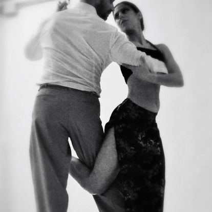 Un uomo e una donna ballano insieme, entrambi vestiti con abiti da ballo formali. L'immagine, che emana un'atmosfera da Buena Onda Tango, è in bianco e nero, evidenziando il loro movimento aggraziato.
