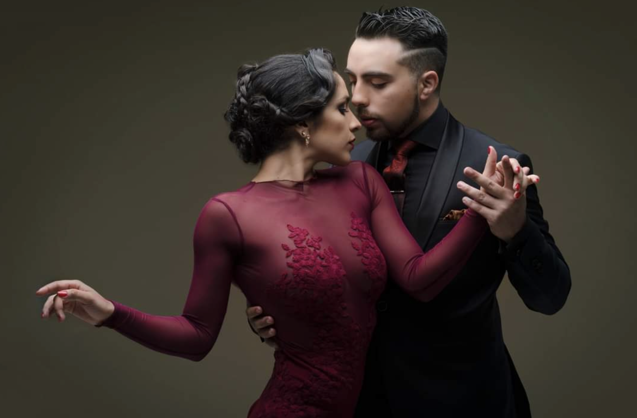 Una coppia in abiti eleganti esegue una posa di danza ravvicinata e drammatica su uno sfondo semplice.